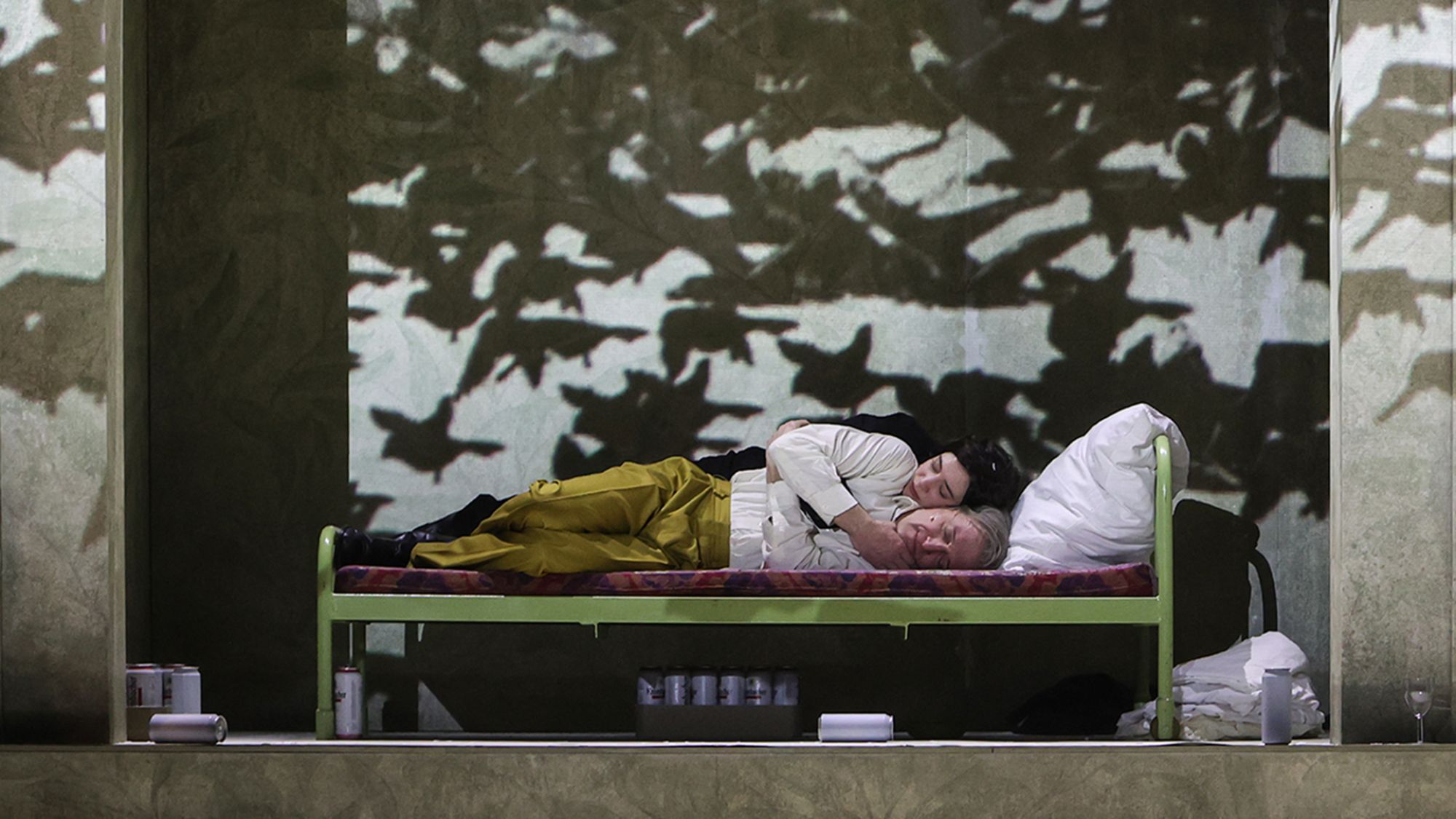 | | Zwei Menschen liegen seitlich nebeneinander auf einem Bett, umgeben von eine Projektion, die einen Vogelschwarm zeigt.