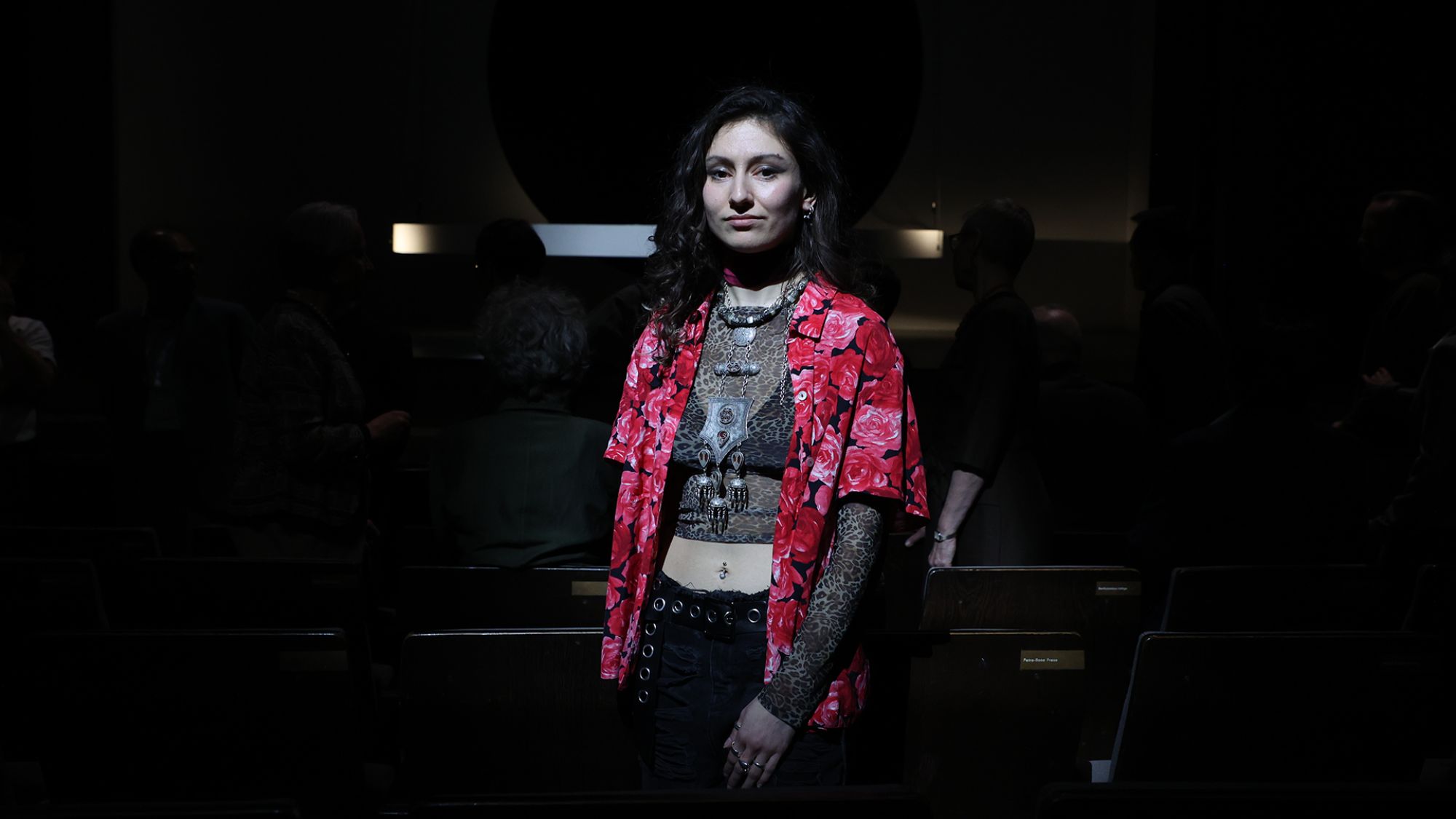 | | Eine Person steht vor dunklem Hintergrund und schaut in die Kamera.