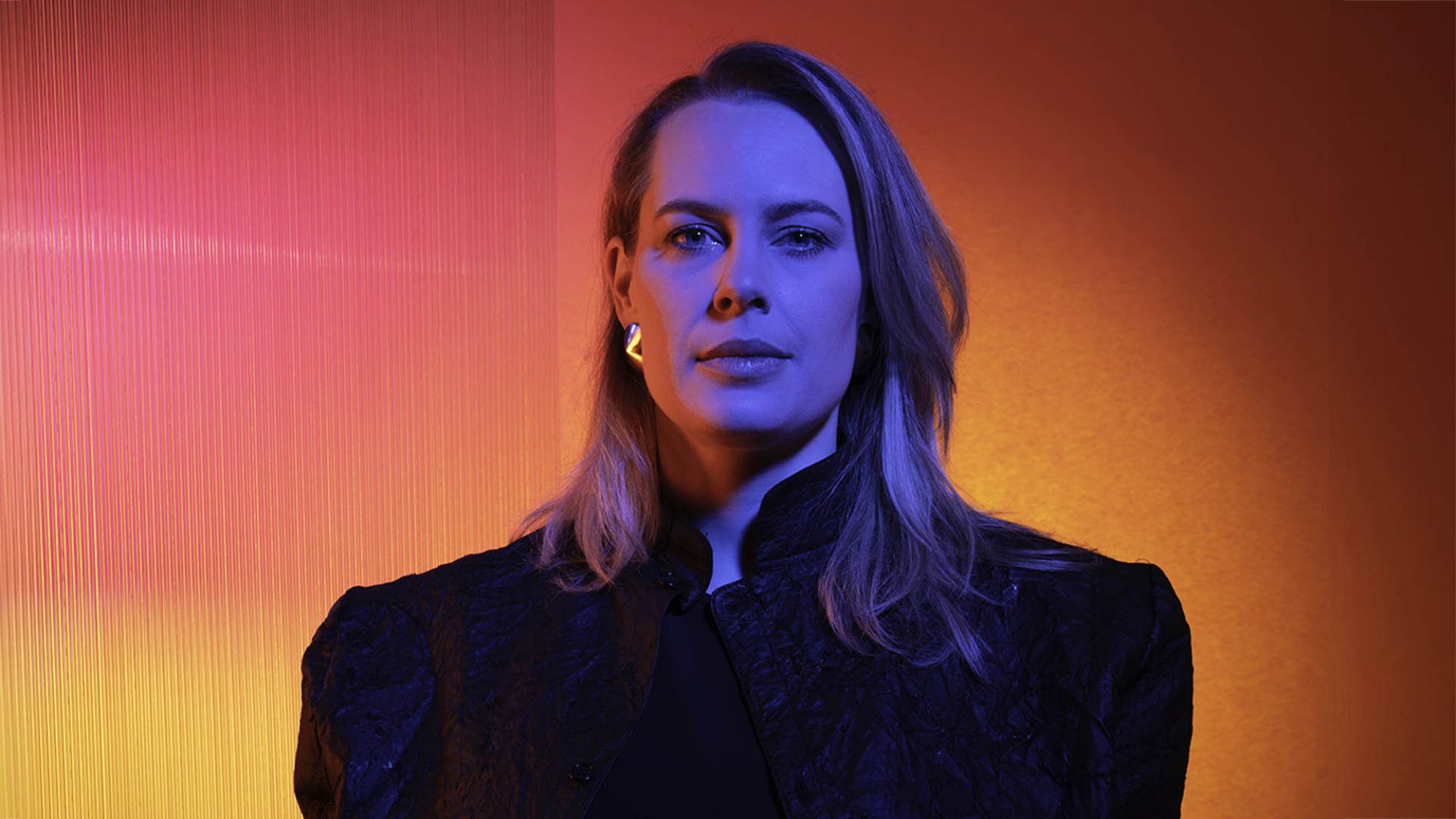 | | HfK: Berderow, Kirchner, Olker Eine Frau mit blonden Haaren schaut in die Kamera. Sie trägt ein schwarzes Oberteil. Der Hintergrund ist rosa-rot.