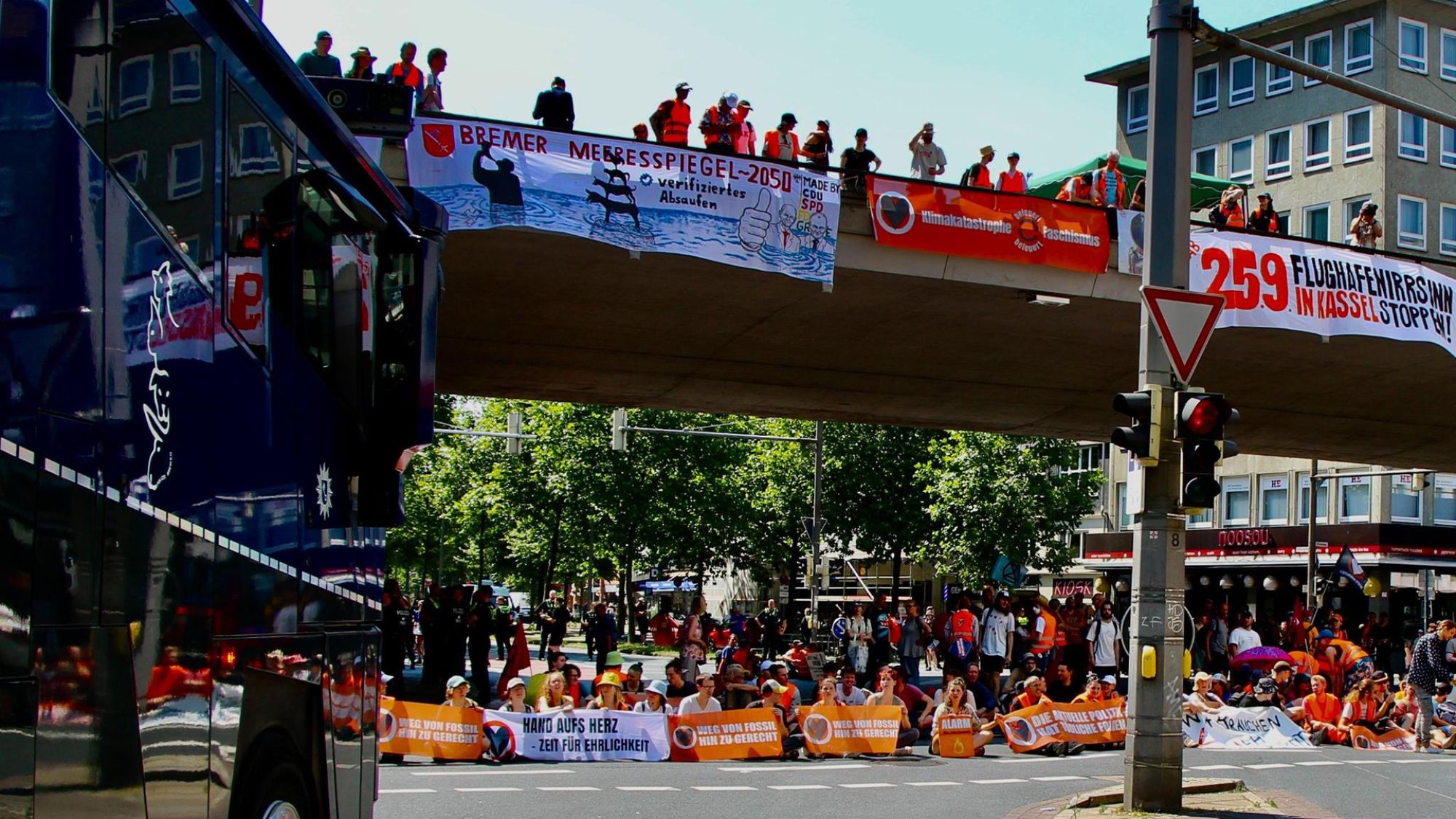 | | Auf einer Straße sitzen viele Menschen mit orangenen Bannern. Auch von der Brücke über den Menschen hängen Banner mit politischen Botschaften.