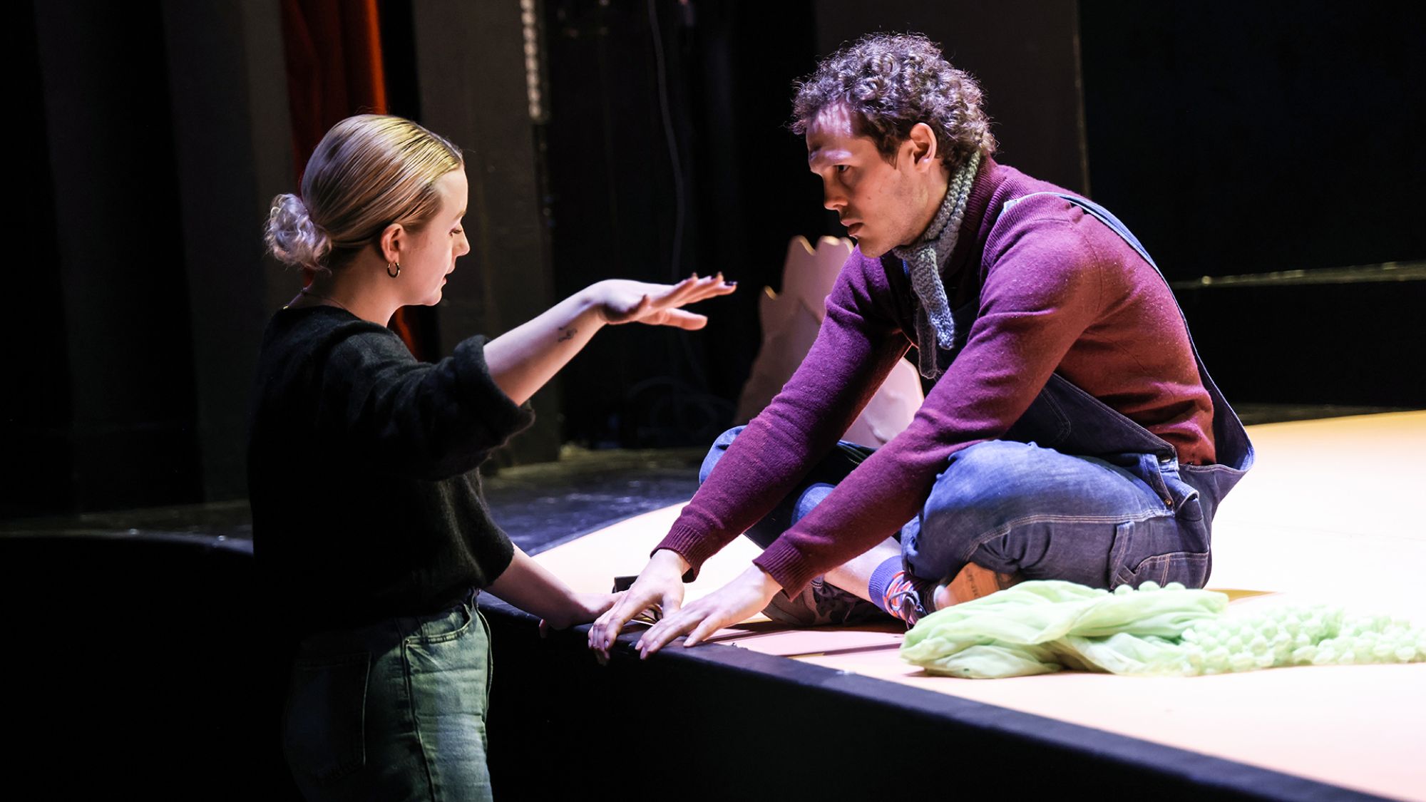 | | Ein Mann sitzt auf der Bühnenkante. Vor ihm steht eine Frau. Die beiden schauen sich an.