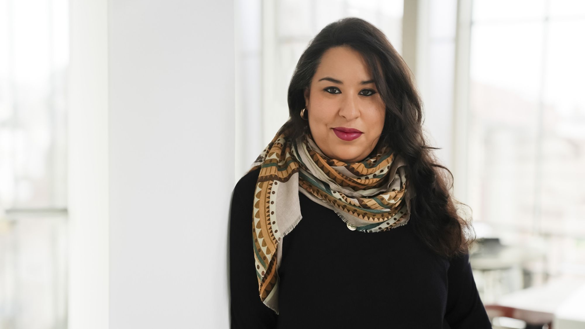 | | Eine Frau blickt in die Kamera. Der Hintergrund ist verschwommen.