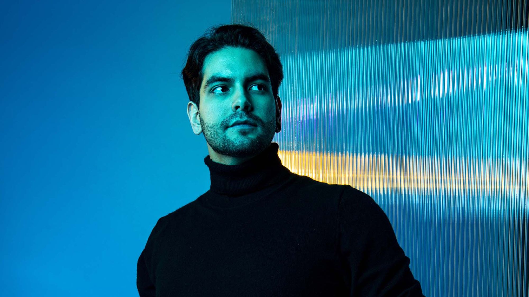 | | HfK: Berderow, Kirchner, Olker Ein Mann steht vor einer blauen Wand. Er hat kurze schwarze Haare und trägt einen Rollkragenpullover.