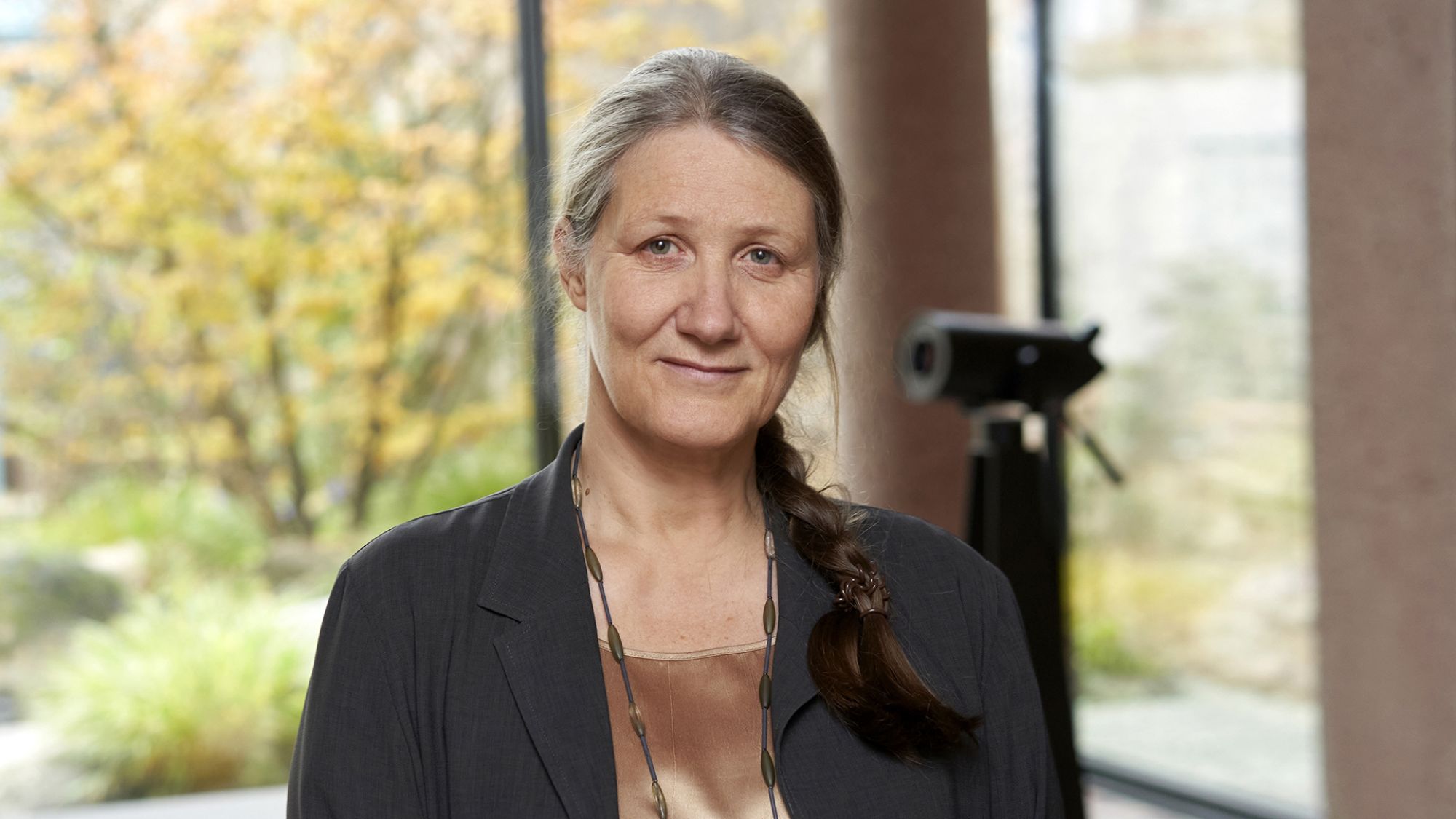 | | Alexander Paul Englert Eine Frau schaut in die Kamera. Sie trägt eine dunkle Bluse und eine Kette um den Hals. Ihre Haare sind zu einem Zopf geflochten.