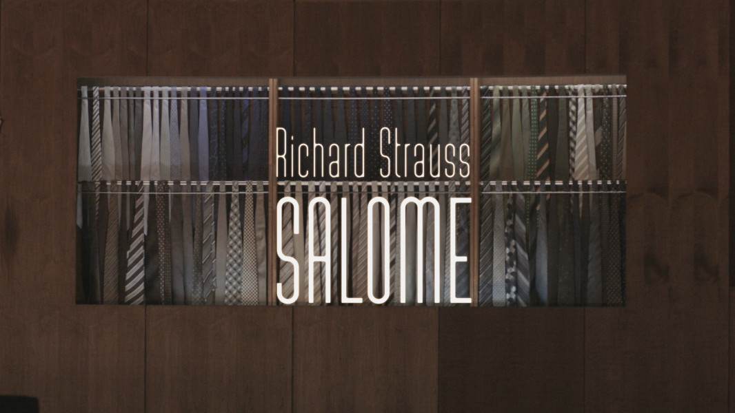 Dieses Foto ist das Standbild zum Videotrailer mit Stückimpressionen aus Claus Guths Interpretation zu Richard Strauss' SALOME. In eine edle holzvertäfelte Wand ist die beleuchtete Auslage für Herrenkrawatten eingelassen.