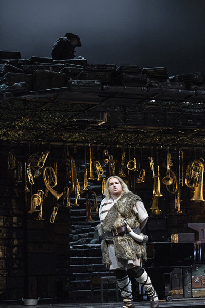 Ein Inszenierungsdetail: Siegfried in einem Kostüm, das an die Uraufführungszeit angelehnt ist, vor einem Raum voller Hörner und Blechblasinstrument.
