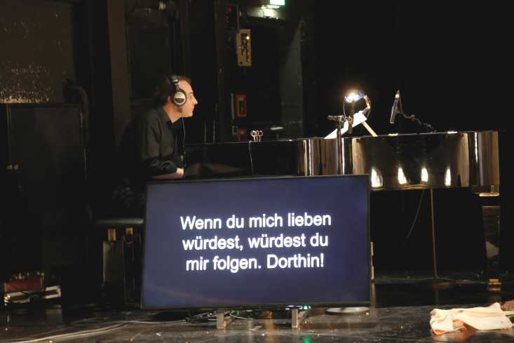Ein Mann mit Kopfhörern am Klavier. Vor ihm ein Monitor mit dem Text, der gesungen wird.