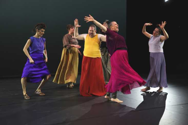 Sechs Personen tanzen wild. Alle tragen Röcke oder Kleider in unterschiedlichen Farben.