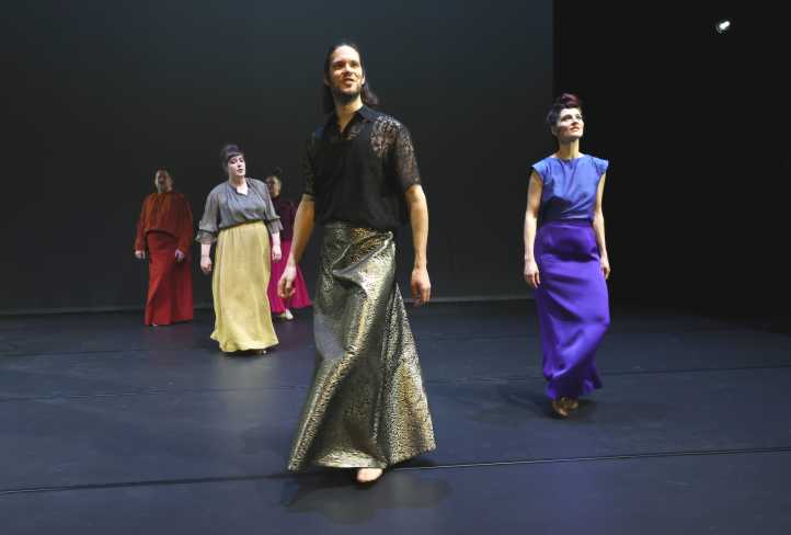 Fünf Personen schreiten über die Bühne. Alle tragen bodenlange Röcke in unterschiedlichen Farben.