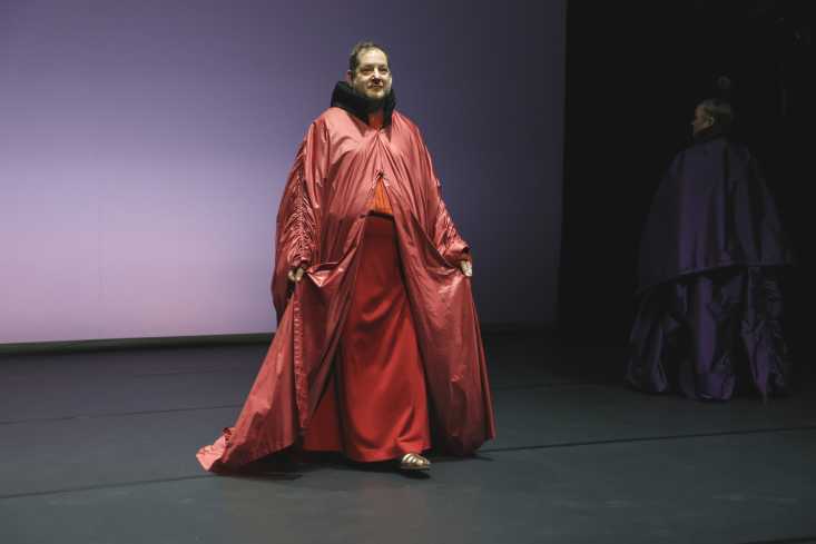 Ein Performer in einem langen roten Mantel kommt auf das Publikum zu.