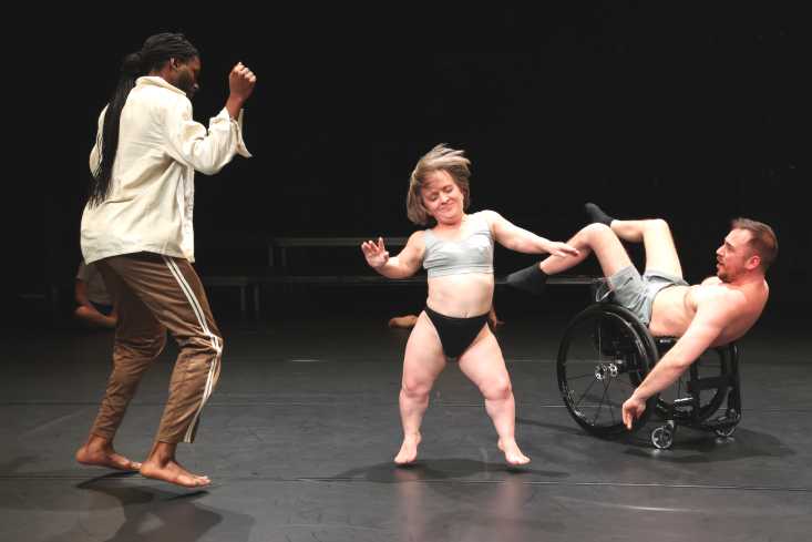 Drei Personen tanzen, eine von ihnen sitzt in einem Rollstuhl.