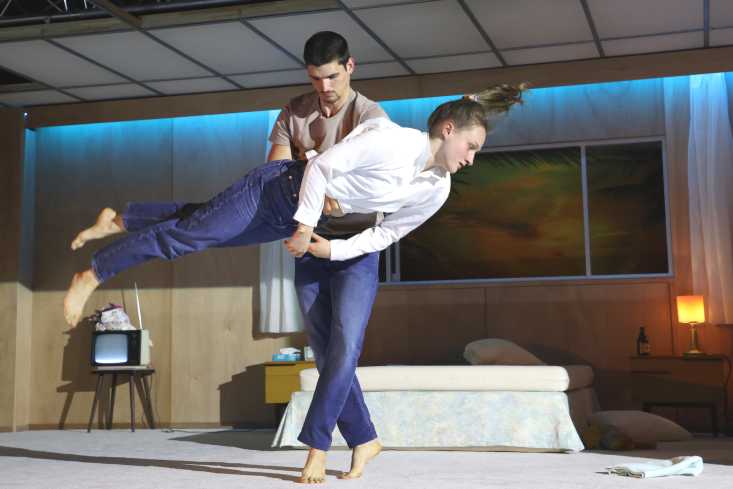 Ein Tänzer hält eine Tänzerin am Bauch fest. Sie schwebt und ist ganz gerade. Ihre Haare fliegen. 