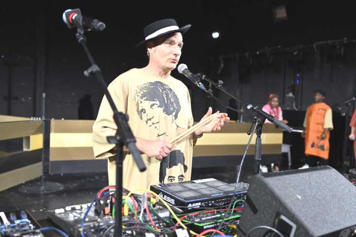 © Knut Klaßen // Ein Musiker steht an einem DJ-PUlt. Er trägt ein langes, beigefarbenes Gewand und einen schwarzen Hut.