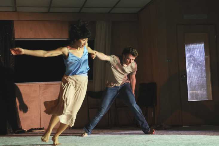 Zwei Menschen halten sich mit ausgebreiteten Armen an den Händen fest. Die Tänzerin ist mitten in der Bewegung fotografiert. 