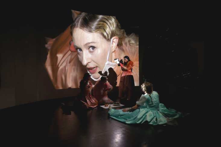 Vier Schauspielerinnen sind auf der Bühne, eine filmt das Gesicht einer anderen. Deren Gesicht ist groß auf eine Wand projeziert.