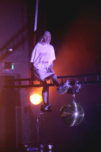 Ein Schauspieler schwebt auf einer Traverse über die Bühne. Er trägt ein übergroßes T-Shirt mit Kapuze und Fellhausschuhe. 