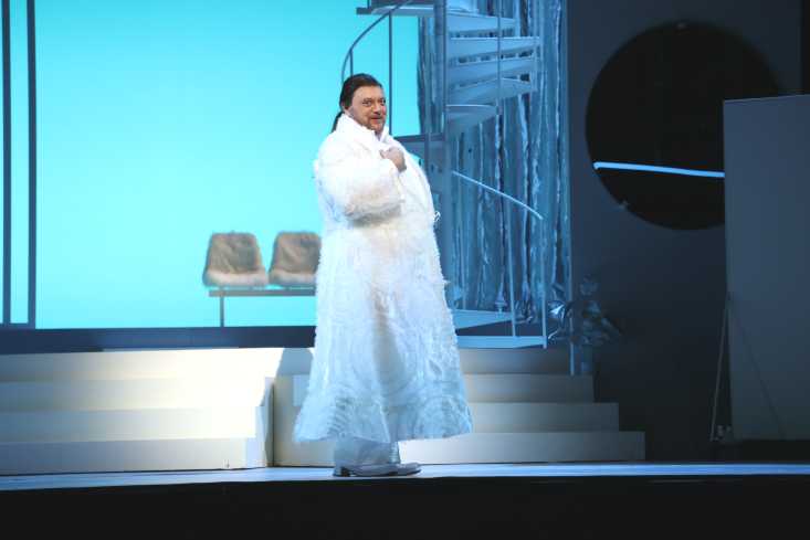 Ein Sänger steht in einem langen weißen Mantel im Scheinwerferlicht.