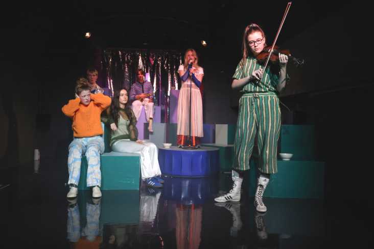 Sechs junge Akteure sind auf der Bühne. Eine singt, eine spielt Geige. Eine hält sich die Ohren zu.