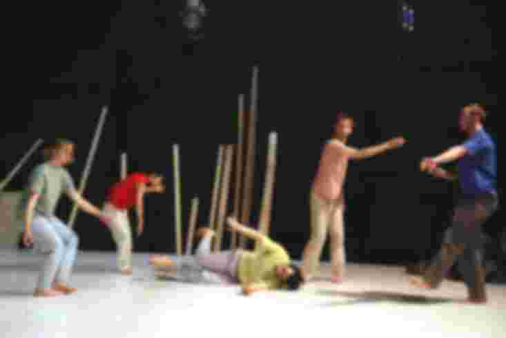 Fünf Menschen in bunter Alltagskleidung tanzen. Einer von ihnen liegt in der Mitte der Bühne auf dem Boden.