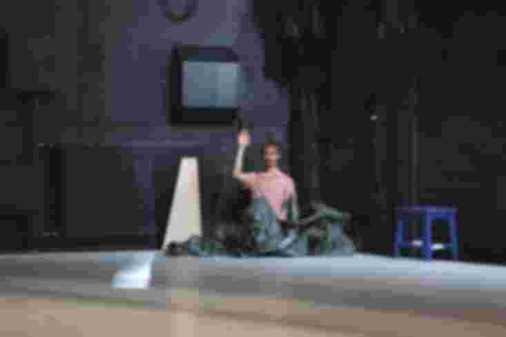 Ein Tänzer kniet in einem großen, aufgebauschten Plastikplane. Er hebt die Hand.