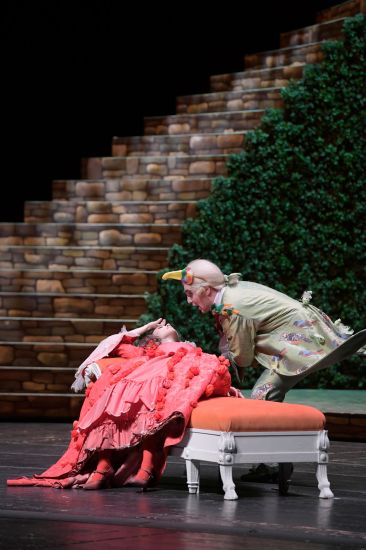 TITLE: Das Märchen von der Zauberflöte
COPYRIGHT: Bettina Stöß Papageno trifft auf Pamina. In einem roten langen Kleid und roten Blumen im Haar liegt sie auf einer Chaiselongue. Papageno beugt sich über sie.