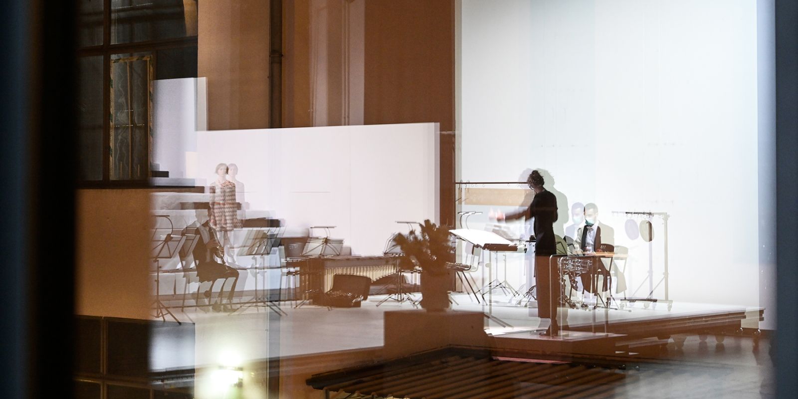 Once to be realised - ©2020 ©Stephan Bögel Auf diesem Foto vermischen sich in einer Art Überblendung architektonische Momente der Tischlerei mit Musiker*innen und einem Dirigenten. Es ist ein sehr atmosphärisches Bild, mit dem wir das Programm der Tischlerei bildlich fassen.