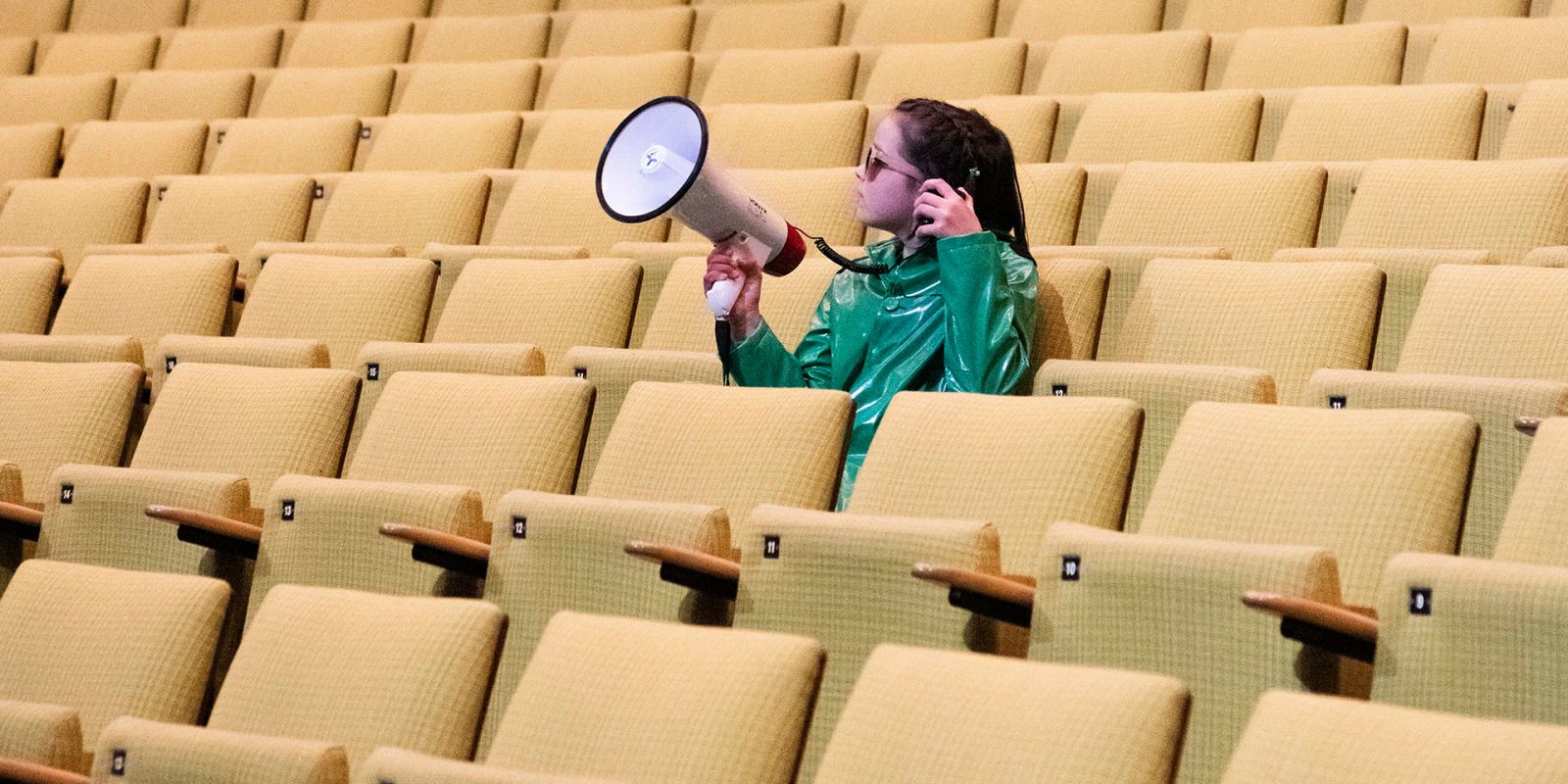 Junge Deutsche Oper 2025/26 - ©S. I. Ein Kind mit Megaphon sitzt in den ansonsten leeren Reihen unseres Parketts.
