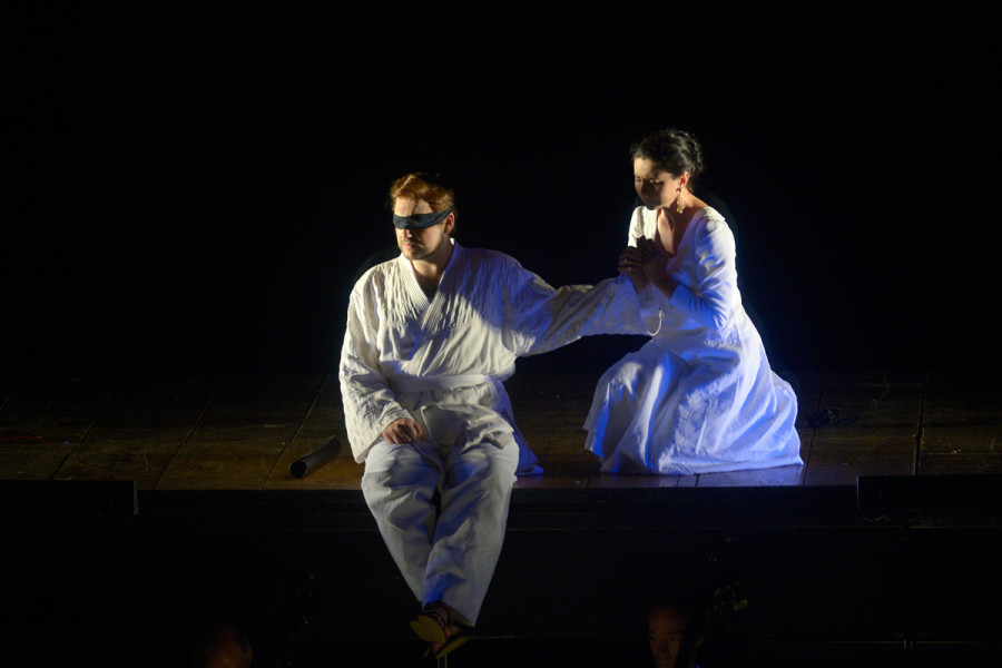 Die Zauberflöte - © Bettina Stöß Tamino sitzt mit verbundenen Augen am Bühnenrand. Neben ihm kniet, seine Hand haltend, Pamina. Sie fleht ihn an. Er blickt - scheinbar teilnahmslos - zur gegenüberliegenden Seite.