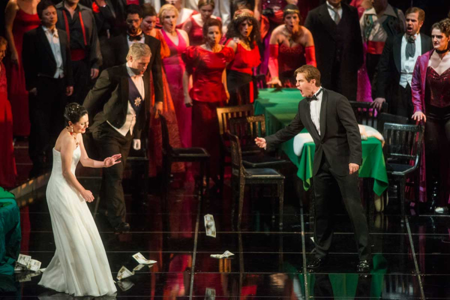 La Traviata - © Marcus Lieberenz Violetta hat Alfredo einen Abschiedsbrief geschrieben und ist in ihr halbseidenes Pariser Leben zurückgekehrt. Bei einem Fest überrascht Alfredo sie und wirft ihr ein Bündel Geld vor die Füße, als ihren Hurenlohn. In ihrem Gesicht spiegelt sich der Schmerz, seines ist zutiefst wütend.