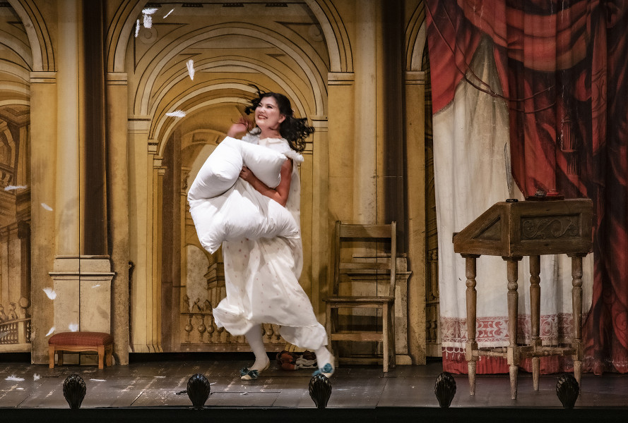 Il barbiere di Siviglia - © Bettina Stöß Die Front des Theaterwagens hat sich geöffnet. Im Inneren zeigt sich in altitalienischer Perspektivmalerei das Wohnzimmer Rosinas. Sie zerreißt vor Glück ihr Kopfkissen, um die Federn auf sich herabschneien zu lassen.