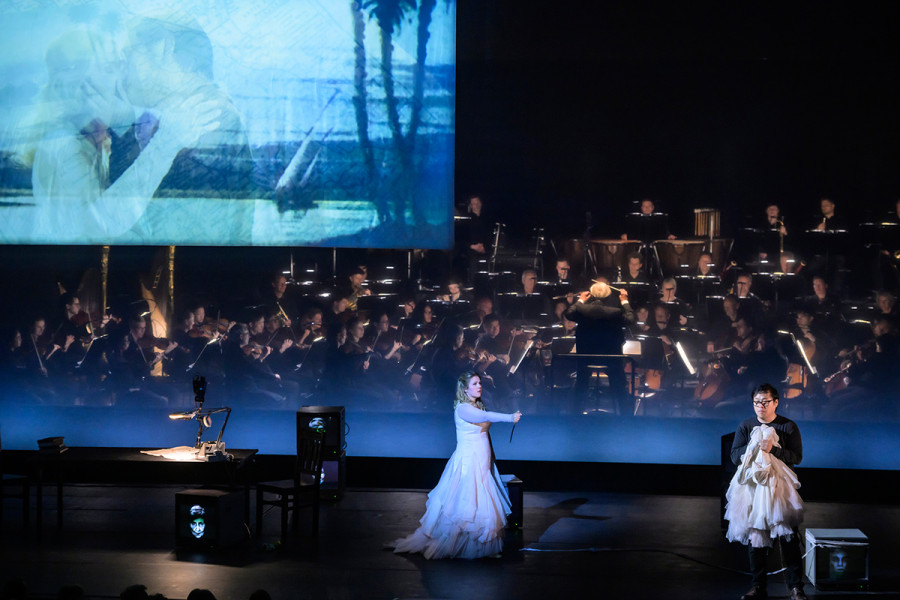 Aida - © Bettina Stöß Auf der Bühne weit von einander getrennt, und Aida immer noch Radames mit dem Messer bedrohend, ist auf der Leinwand nun ein inniger Kuss zwischen Radames und Aida.