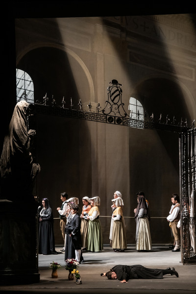 Tosca - © 2023, Bettina Stöß Vor der Madonna liegt Scarpia betend auf dem Kirchenboden. Seine Arme und sein Körper bilden dabei ein Kreuz. Vor den Toren der Kirche schreitet noch immer die Prozession.