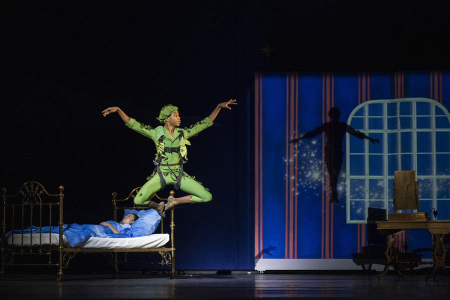 Peter Pan tanzt. Hinter ihm im Bett Wendy. Den Hintergrund bildet ein großes Fenster.