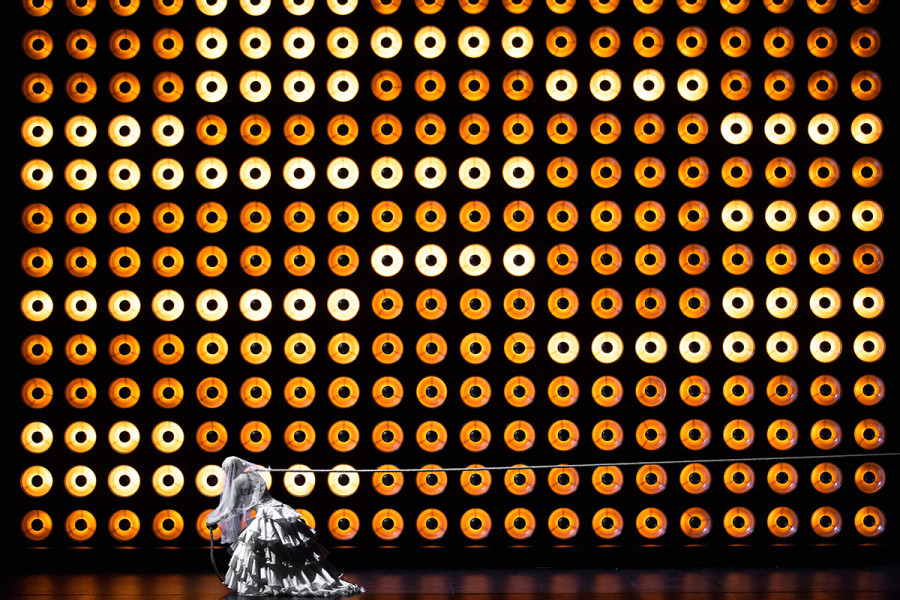 Tristan und Isolde -   © Bernd Uhlig  Vor einer Wand aus zahllosen Lampen zieht Isolde an einem Seil. Sie trägt ein Brautkleid.