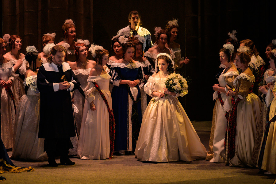 Lucia erscheint im Brautkleid zu ihrer Hochzeit. Sie trägt einen üppigen Straus weißer Rosen. Um sie der Chor, rechts davor ihr Vertrauter Raimondo. Sie sieht traurig aus.