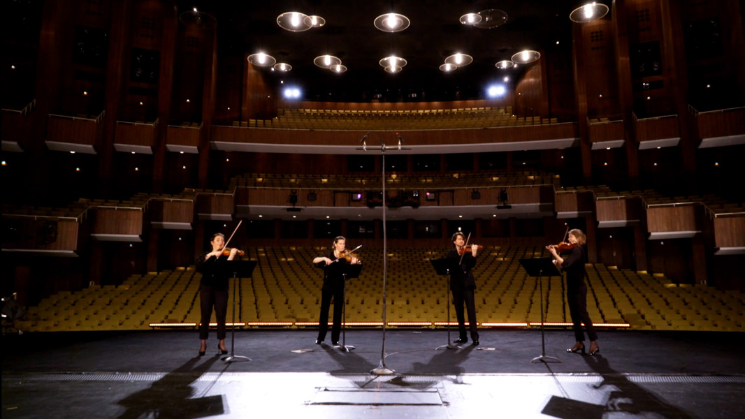 Violinquartett mit Arien aus DIE ZAUBERFLÖTE - © Ruth Tromboukis Dieses Bild ist das Standbild zu einem Video, in dem ein Streichquartett die berühmtesten Arien aus der ZAUBERFLÖTE spielt. Vier Musiker*innen stehen mit dem Rücken zum leeren Saal auf der Bühne der Deutschen Oper Berlin.