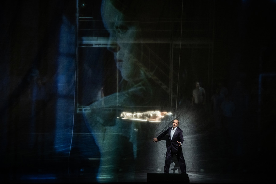 Turandot - © 2023 // Bettina Stöß Calaf steht vor einem Gazevorhang, auf den ein Kinderbild projiziert wird. Hinter der Gaze schläft Turandot. Vor dieser Kulisse erklingt Calafs "Nessun dorma".