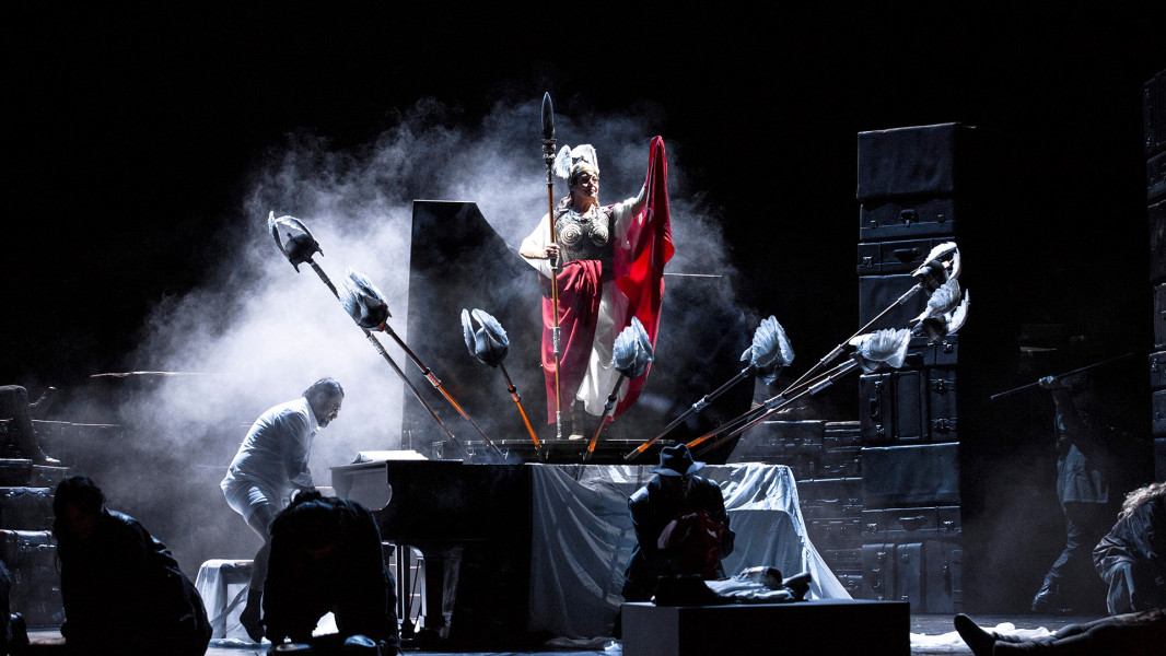 Die Walküre - © Bernd Uhlig Während Wotan auf dem Flügel die Auftrittsmusik vorgibt, steigt aus dem geöffneten Flügel Brünnhilde mit allen Lanzen für die weiteren Walküren auf. Brünnhilde ist in ein mittelalterliches Gewand gekleidet, das das Kostüm der Uraufführung zu zitieren scheint: mit Brustpanzer, Flügelhelm. Sie schlingt ein auffälliges tiefrotes Tuch um sich.
