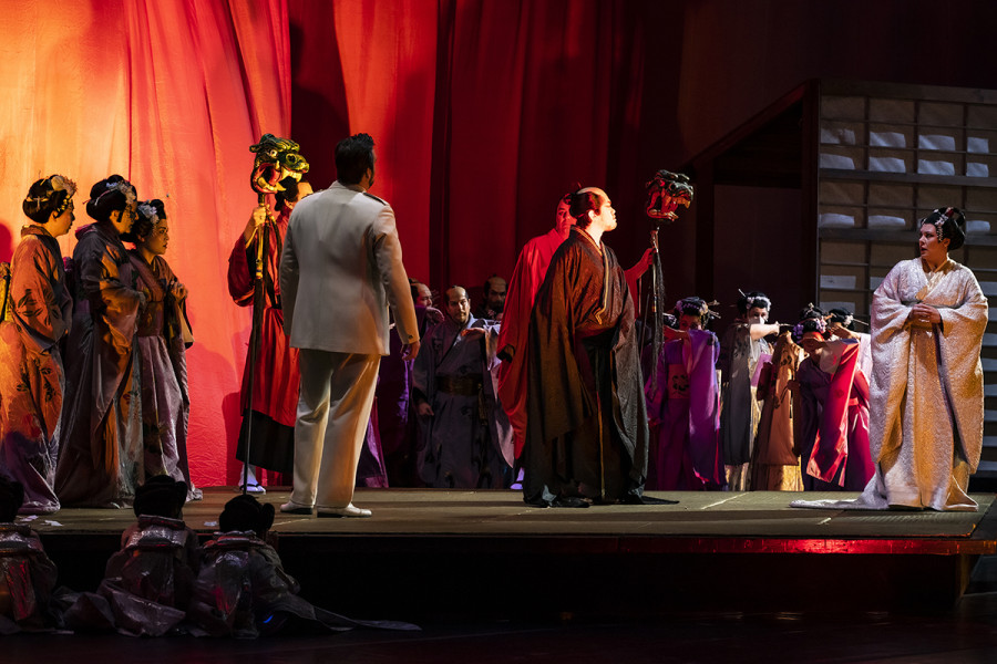 Madama Butterfly - © Bettina Stöß Die Hochzeitszeremonie wird durch ihren Onkel jäh unterbrochen, der Cio-Cio-San verflucht wegen eines Besuches im Missionarshaus. Das bis dahin nachtblaue Bühnenbild wird in flackernde Feuerfarben getaucht.