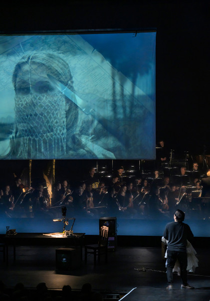 Aida - © Bettina Stöß Auf der Videoleinwand erscheint eine Fatamorgana gleich ein Bild von Aida. Verträumt sieht es Radames.