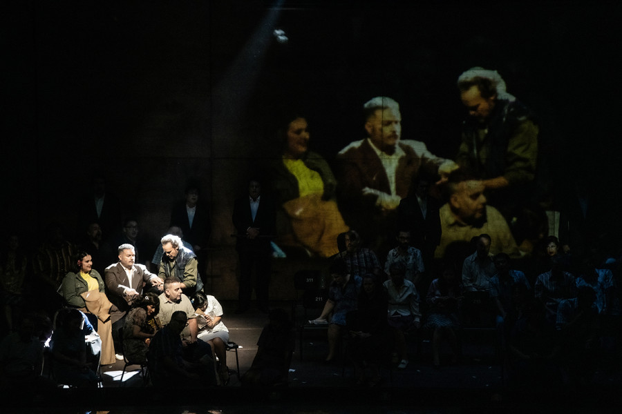 Turandot - © 2023 // Bettina Stöß In der linken Ecke sitzen Timur, Liú und Calaf. Das Bild wird mit einer Livekamera auf einen Gazevorhang übertragen.
