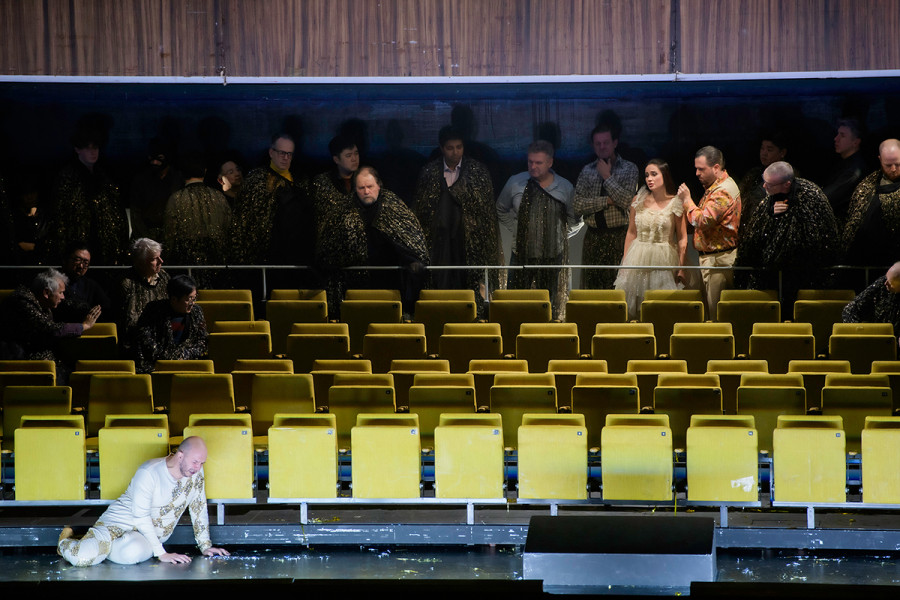Rigoletto - © Bettina Stöß Im Bühnenhintergrund drängen sich noch immer die Höflinge, um nichts von der Erniedrigung des ungeliebten Hofnarren zu versäumen. In Begleitung von Matteo Borsa betritt Gilda den Saal. Vor der ersten Stuhlreihe kniet Rigoletto zusammengesunken vor Verzweiflung.
