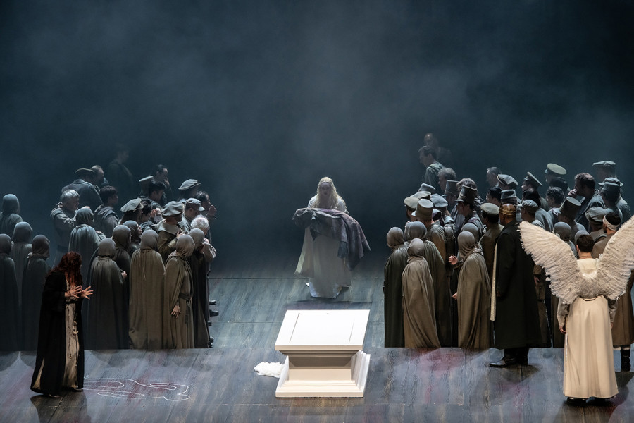 Lohengrin - © Bettina Stöß Links und rechts auf stehen, vom Punlikum abgewandt Ortrud und Lohengrin. Der Chor bildet eine Gasse, durch die Elsa auftritt mit der Leiche ihres kleinen Bruders im Arm. Ein großer Sarkophag dominiert die Bühne.