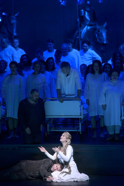 Tannhäuser und der Sängerkrieg auf Wartburg - © Bettina Stöß Venus/Elisabeth empfängt Tannhäuser in ihren Armen, hinter ihnen Wolfram, von der Situation sichtlich überfordert. Der Chor hat sich aus den Betten erhoben, hinter dem Chor sind wieder die Ritter sichtbar.