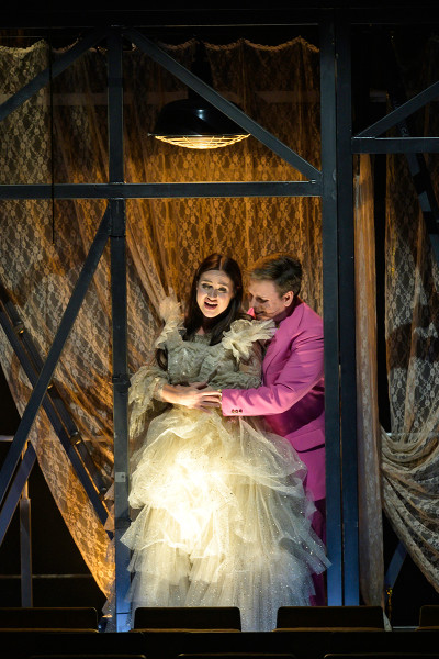 Rigoletto - © Bettina Stöß Gilda und der Herzog im Duett in Gildas Zimmer. Sie trägt ihr Kleid aus Gardinenstoff, er den Anzug in grellem Pink. Er hält sie im Arm.