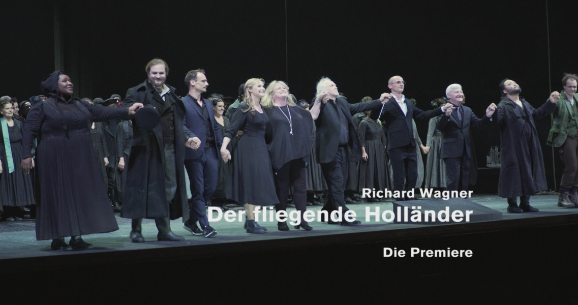 Dieses Bild ist das Standbild zum Video "Nach der Premiere". Es ist der Verbeugungsapplaus von Sänger*innen und Regieteam.
