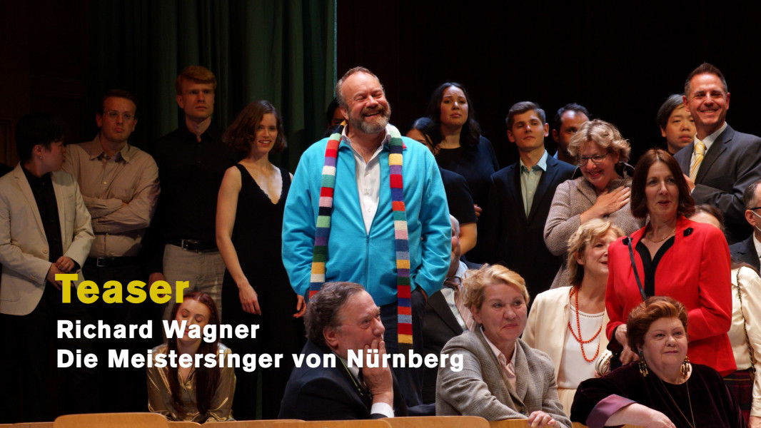 Dieses Bild ist das Standbild für einen Kurzteaser. Hans Sachs steht lachend zwischen dem Chor.