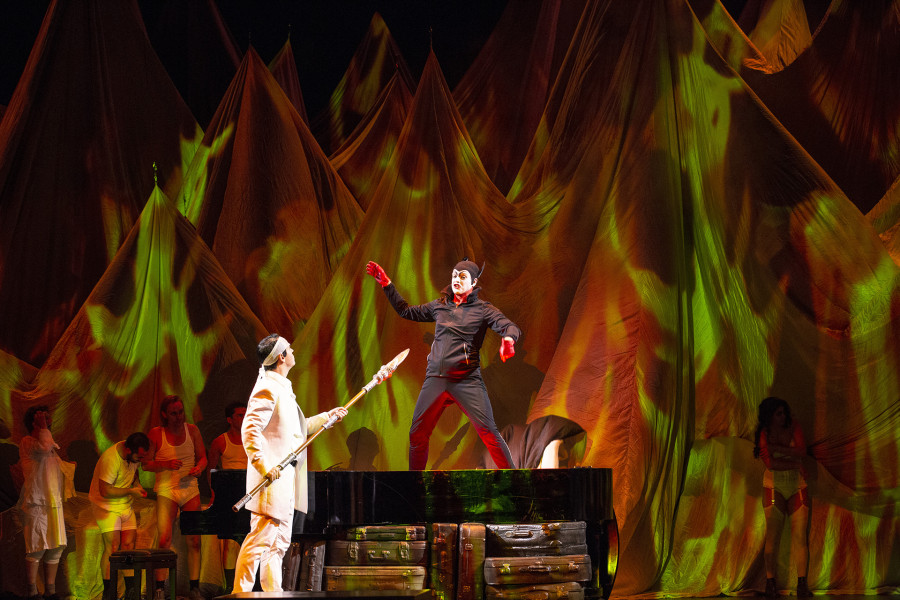 Das Rheingold - © Bernd Uhlig Loge und Wotan im Gespräch. Das Gebirge hinter ihnen scheint in Flammen zu stehen. Wotan schaut drohend auf Loge, dem der Sarkasmus ins Gesicht geschrieben steht.