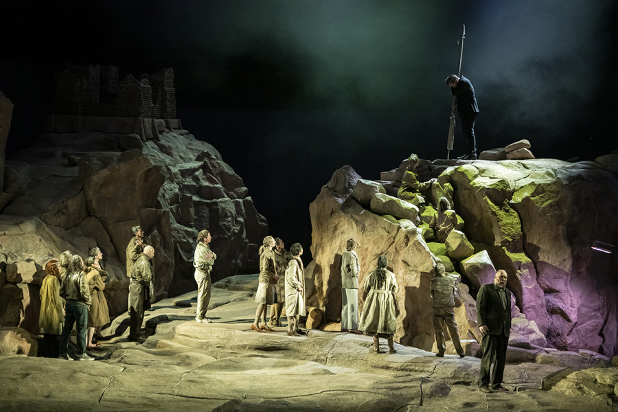 Parsifal - © Bettina Stöß Parsifal findet zurück zur Gralsburg. In seinem schwarzen Anzug steht er mit verhüllter Lanze rechts auf dem Plateau. Unten Stehen Gurnemanz und einige Gralsritter.