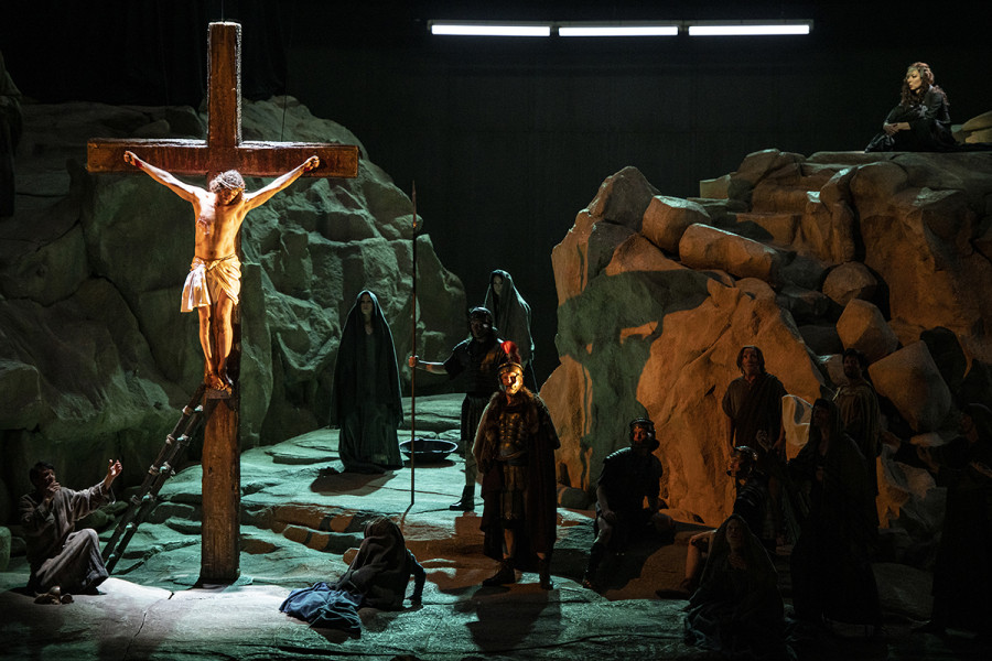 Eine Szene aus der inszenierten Ouvertüre: Jesus hängt am Kreuz. Um ihn herum römische Soldaten und Jünger sowie Frauen. Rechts auf dem Bergplateau sitzt Kundry.